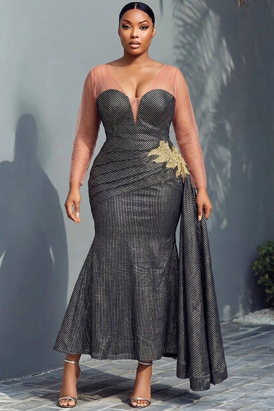 Woman wearing black and gold metallic stripe mermaid gown with sheer nude illusion sweetheart neckline, sheer long sleeves, ruched diagonal skirt, gold lace floral appliqué at hip and sweeping side cape train