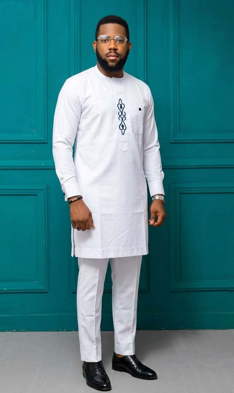 Man wearing a white Nigerian Senator two-piece suit with navy blue chain embroidery on chest placket, paired with black Oxford shoes