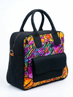 Side angle view of black Ankara bowling bag with vivid purple, orange and teal abstract fluid art print panel, padded top handles and front flap pocket