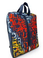 Angled front view of Ankara print laptop backpack showing full abstract batik print, front zip pocket and padded backpack straps