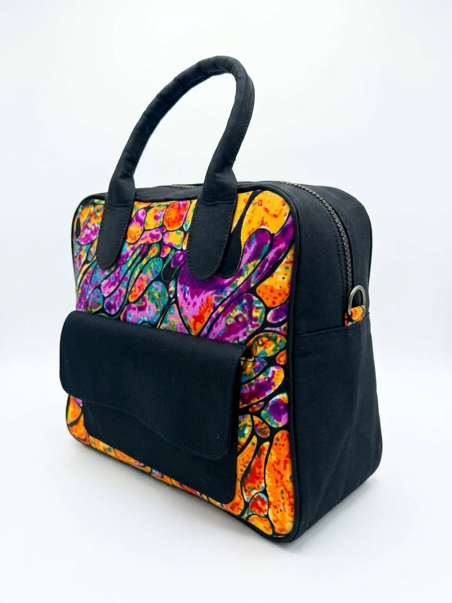Three-quarter view of black Ankara abstract bowling bag showing full fluid art print panel, zip-top closure and side D-ring attachment
