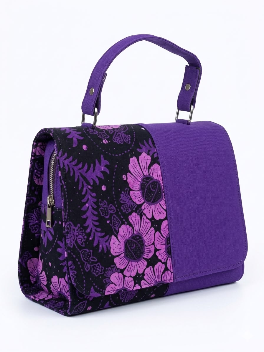 Side angle view of purple Ankara floral satchel with pink and magenta bloom print panel, single riveted top handle and side zip pocket